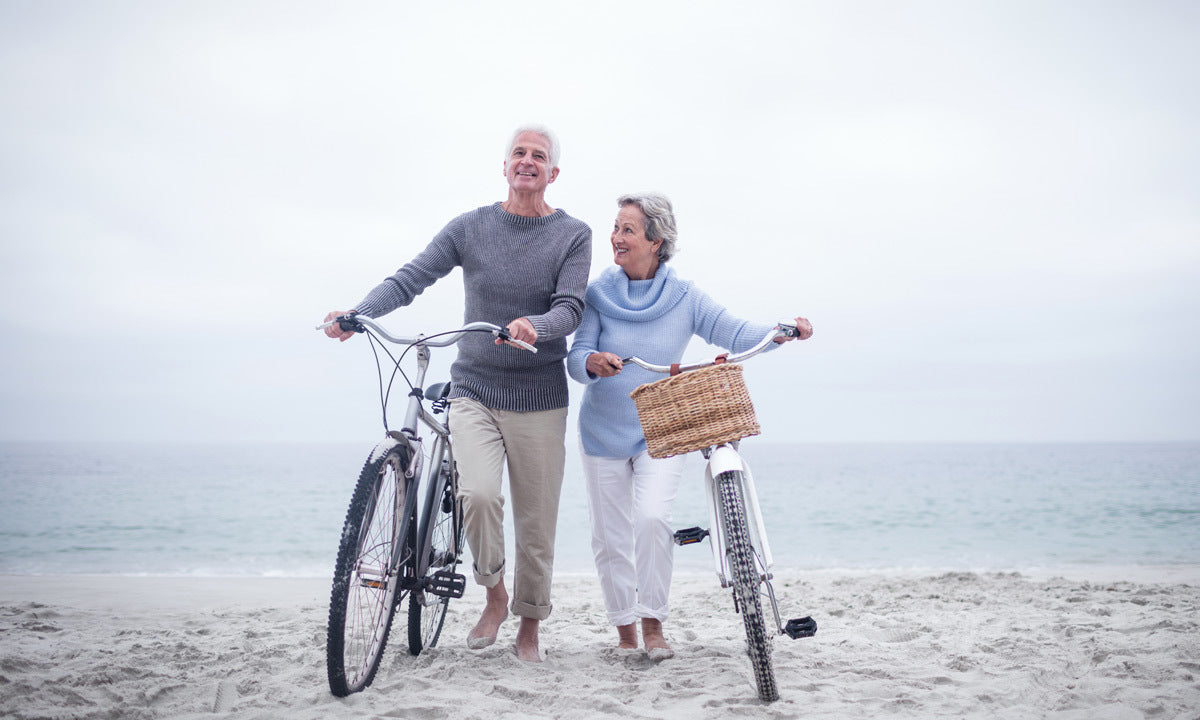 senior couple walking bikes on beach