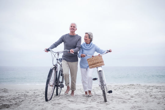 senior couple walking bikes on beach